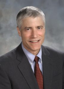 Picture of Peter Netland wearing a red tie, blue shirt, and dark suitcoat. 