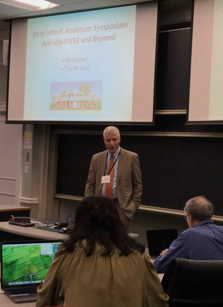 Peter Netland stands in front of a large screen. He is speaking to attendees at the conference.